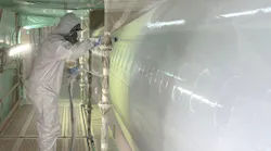 A person in a full-coverage PPE suit applying a clear coat to an airplane with a sprayer
