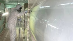 A person in a full-coverage PPE suit applying a clear coat to an airplane with a sprayer A person in a full-coverage PPE suit applying a clear coat to an airplane with a sprayer