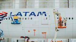 Technicians in lifted platforms applying a coating to a white airplane with text on it that reads: LATAM Technicians in lifted platforms applying a coating to a white airplane with text on it that reads: LATAM