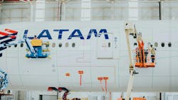 Technicians in lifted platforms applying a coating to a white airplane with text on it that reads: LATAM Technicians in lifted platforms applying a coating to a white airplane with text on it that reads: LATAM
