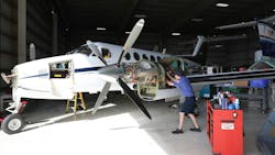 A technician working on an airplane engine that's attached to a small white airplane, with a large toolbox in the forefront A technician working on an airplane engine that's attached to a small white airplane, with a large toolbox in the forefront