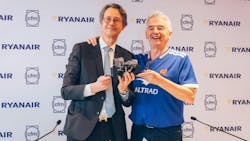 Two men standing and smiling at the camera with one holding a piece of machinery Two men standing and smiling at the camera with one holding a piece of machinery