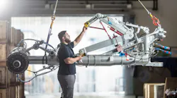 A technician working on a piece of airplane landing gear that's being suspended in the air by cables