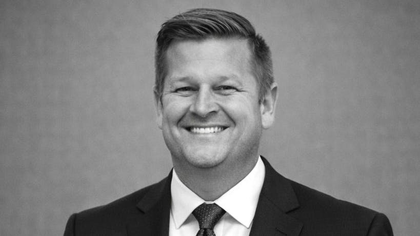 A black-and-white photo of a man wearing a suit and tie smiling at the camera