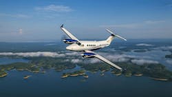 A white airplane with blue accents flying over a body of water with islands in it A white airplane with blue accents flying over a body of water with islands in it