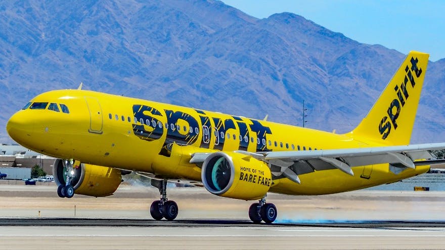 A yellow airplane with the word 'Spirit' printed on it parked on a tarmac in front of mountains