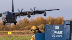 A black military airplane landing in front of a person wearing military fatigues and standing behind a sign that reads: LAST Armor QinetiQ A black military airplane landing in front of a person wearing military fatigues and standing behind a sign that reads: LAST Armor QinetiQ