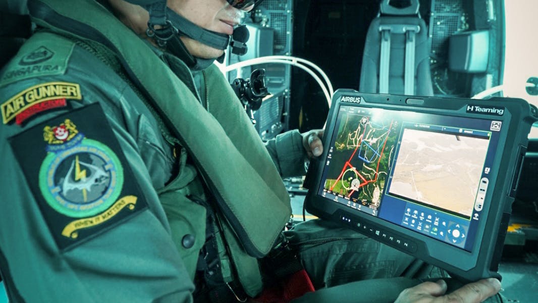 An air crew member in an Air Gunner uniform holding a tablet that shows maps and data