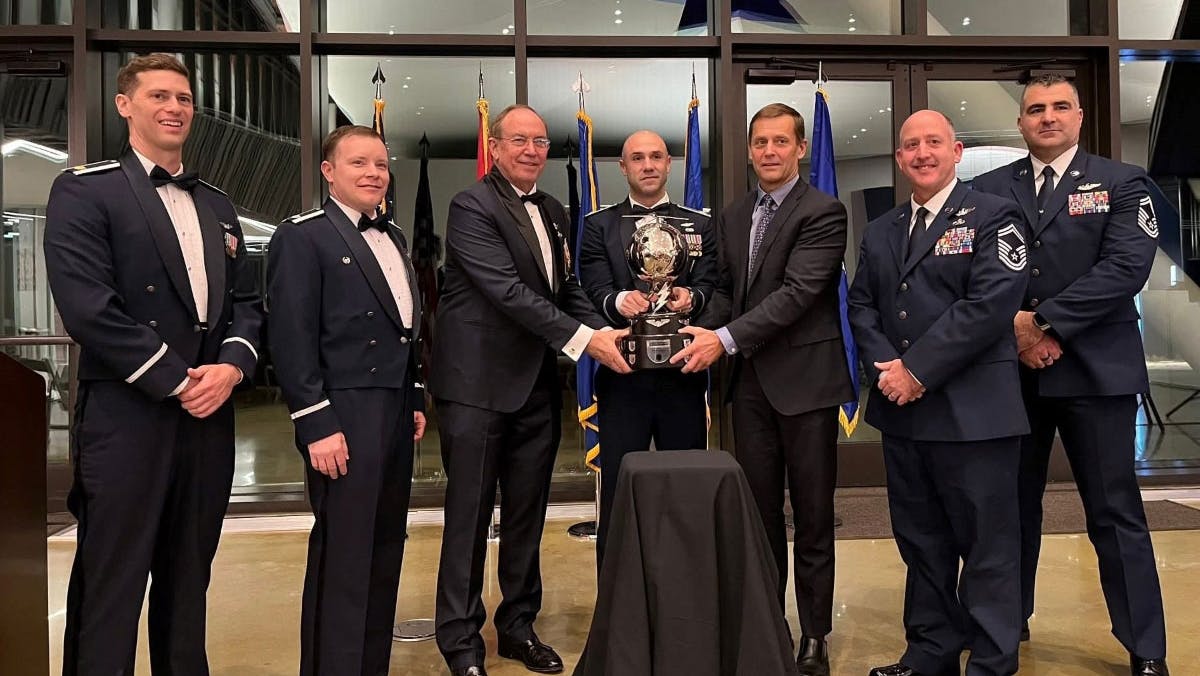 A group of men in formal military dress smiling at the camera and holding a trophy