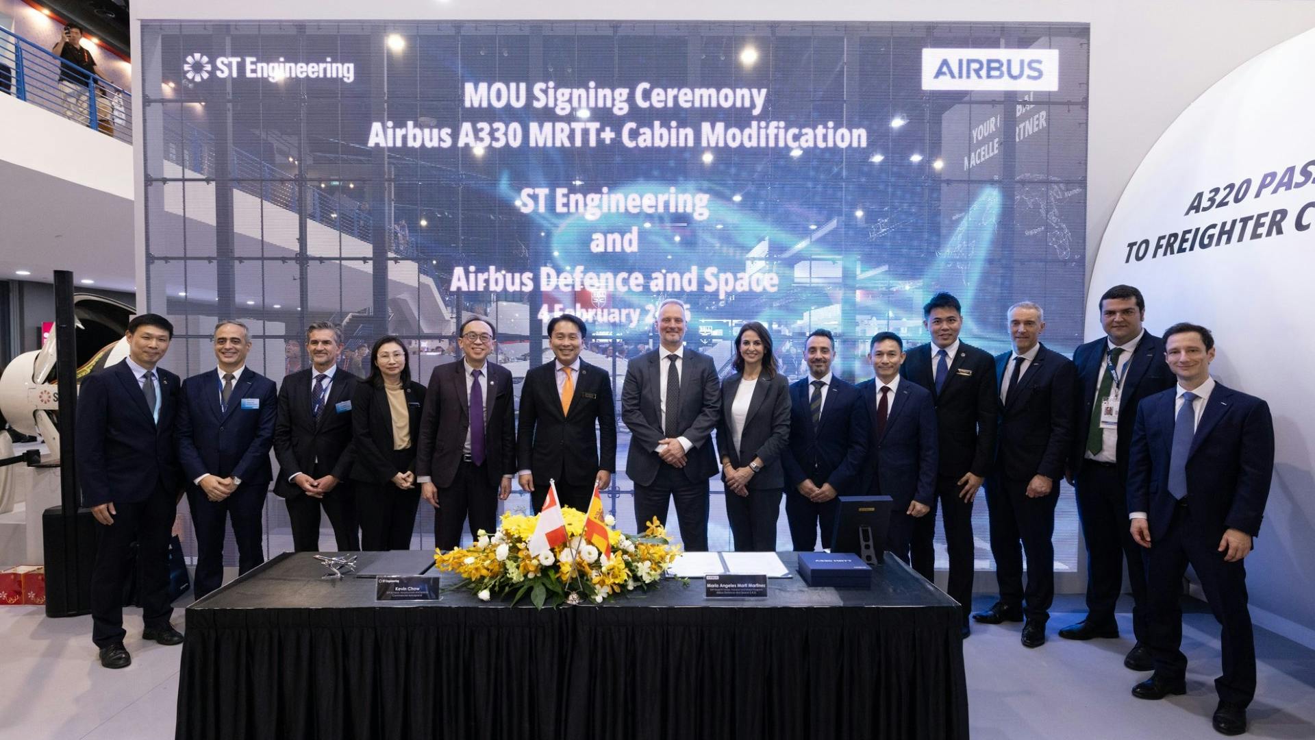 A large group of professionals wearing suits standing behind a table and in front of a backdrop that reads: MOU Signing Ceremony Airbus A330 MRTT+ Cabin Modification ST Engineering and Airbus Defence and Space
