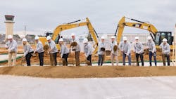 A group of professionals business attire and hard hats standing in a line holding shovels in front of a pile of soil, simulating a groundbreaking A group of professionals business attire and hard hats standing in a line holding shovels in front of a pile of soil, simulating a groundbreaking