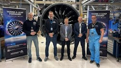 A group of men wearing ID badges standing in front of a detached aircraft engine next to signs that read: Take a leap forward A group of men wearing ID badges standing in front of a detached aircraft engine next to signs that read: Take a leap forward