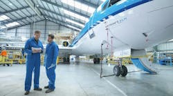 Two aircraft maintenance technicians wearing blue uniforms looking at a stack of papers while standing next to a blue and white airplane in a maintenance hangar Two aircraft maintenance technicians wearing blue uniforms looking at a stack of papers while standing next to a blue and white airplane in a maintenance hangar