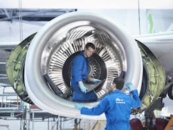 Two aircraft maintenance technicians wearing blue uniforms working inside an aircraft engine Two aircraft maintenance technicians wearing blue uniforms working inside an aircraft engine