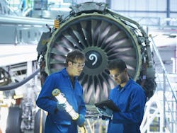 Two aircraft maintenance technicians wearing blue uniforms standing next to an aircraft engine while looking at a tablet screen Two aircraft maintenance technicians wearing blue uniforms standing next to an aircraft engine while looking at a tablet screen