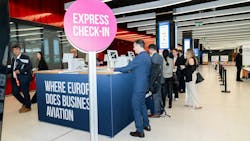 A line of professionals in business attire standing at a booth with a sign that says 'Express Check-In Where Europe Does Business Aviation' A line of professionals in business attire standing at a booth with a sign that says 'Express Check-In Where Europe Does Business Aviation'