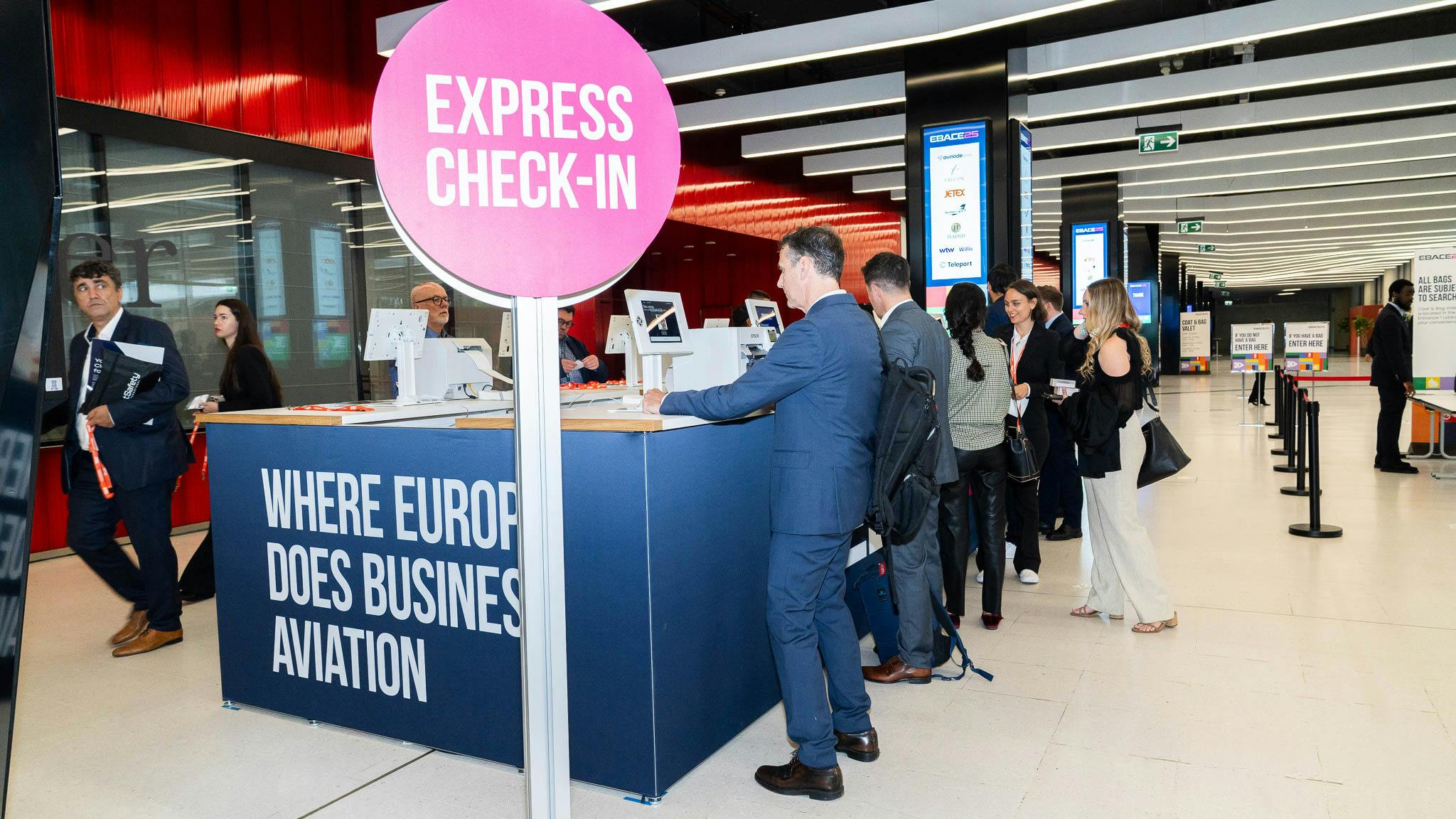 A group of professionals in business attire standing in line at a desk with a sign that reads: Express Check-In Where Europe Does Business Aviation