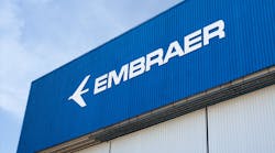 The side of a building with a beige wall and a dark blue sign with white lettering that reads: EMBRAER The side of a building with a beige wall and a dark blue sign with white lettering that reads: EMBRAER