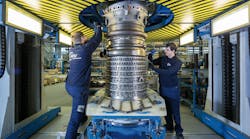 Two maintenance technicians wearing dark blue uniforms working on a large metal engine Two maintenance technicians wearing dark blue uniforms working on a large metal engine