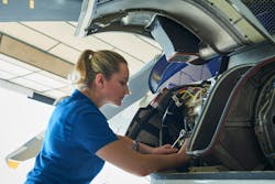 A woman wearing a blue shirt working on an aircraft engine that's open A woman wearing a blue shirt working on an aircraft engine that's open