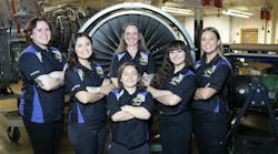 A group of female aircraft maintenance technicians wearing uniforms standing in front of an airplane engine and smiling at the camera A group of female aircraft maintenance technicians wearing uniforms standing in front of an airplane engine and smiling at the camera
