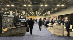 The floor of an exhibition hall with rows of tables and stalls, with professionals in business attire walking around the booths The floor of an exhibition hall with rows of tables and stalls, with professionals in business attire walking around the booths