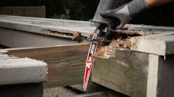 A pair of hands wearing black gloves using a red and white saw blade to cut through a piece of wood A pair of hands wearing black gloves using a red and white saw blade to cut through a piece of wood