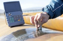 A hand holding a non-destructive testing device up to a large piece of metal A hand holding a non-destructive testing device up to a large piece of metal
