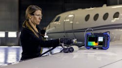 A woman wearing gloves and other PPE using a non-destructive testing device to inspect an airplane, with a handheld part and a screen A woman wearing gloves and other PPE using a non-destructive testing device to inspect an airplane, with a handheld part and a screen
