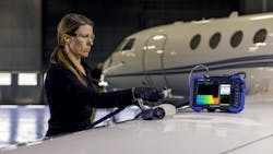A woman wearing gloves and other PPE using a non-destructive testing device to inspect an airplane, with a handheld part and a screen A woman wearing gloves and other PPE using a non-destructive testing device to inspect an airplane, with a handheld part and a screen