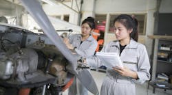 Two female aircraft maintenance technicians wearing gray uniforms working on an open aircraft near the propeller Two female aircraft maintenance technicians wearing gray uniforms working on an open aircraft near the propeller