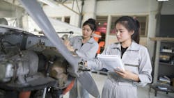 Two female aircraft maintenance technicians wearing gray uniforms working on an open aircraft near the propeller Two female aircraft maintenance technicians wearing gray uniforms working on an open aircraft near the propeller