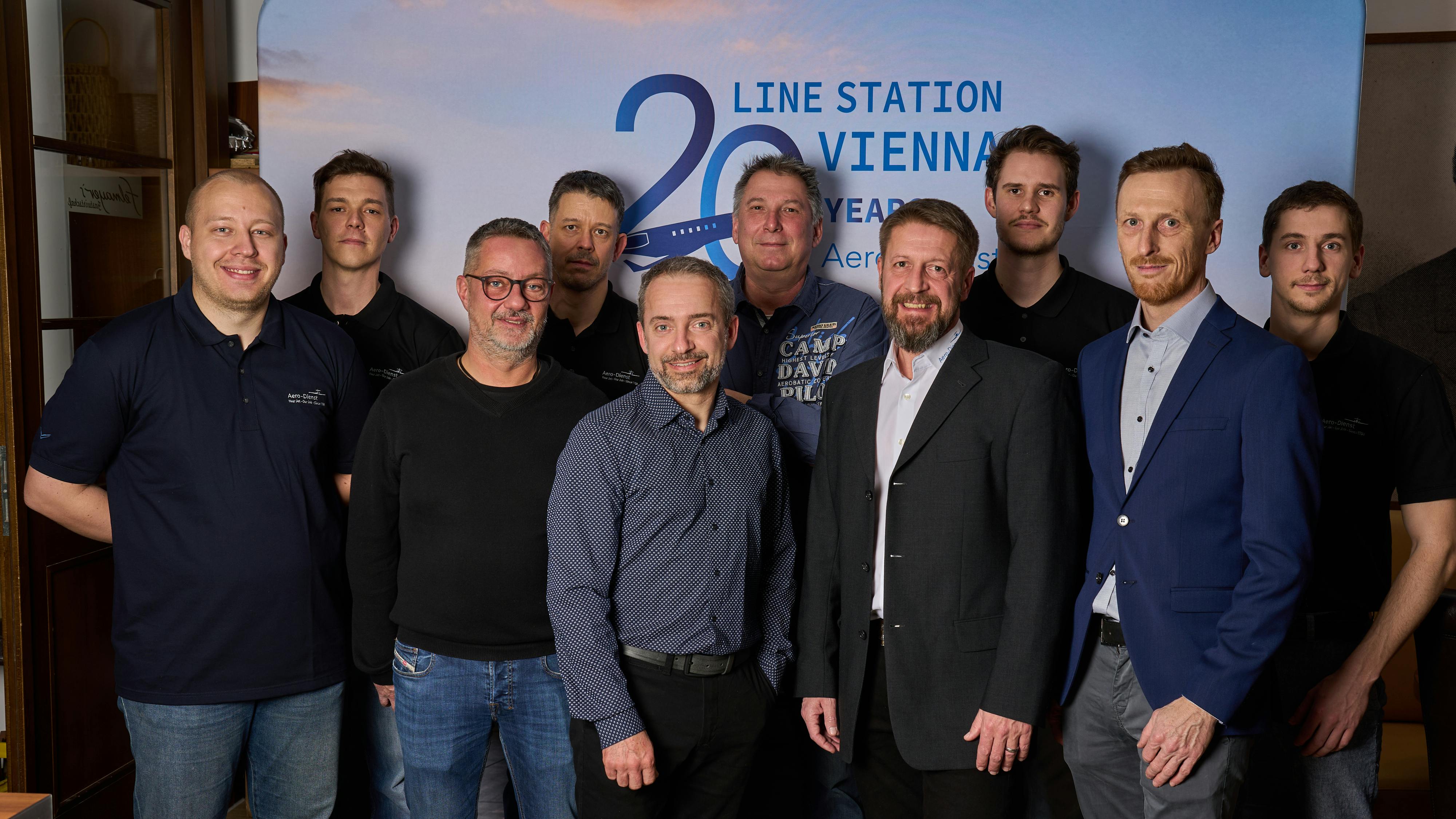 A group of professionals in varying styles of dress standing in front of a backdrop that reads: LINE STATION VIENNA 20 YEARS