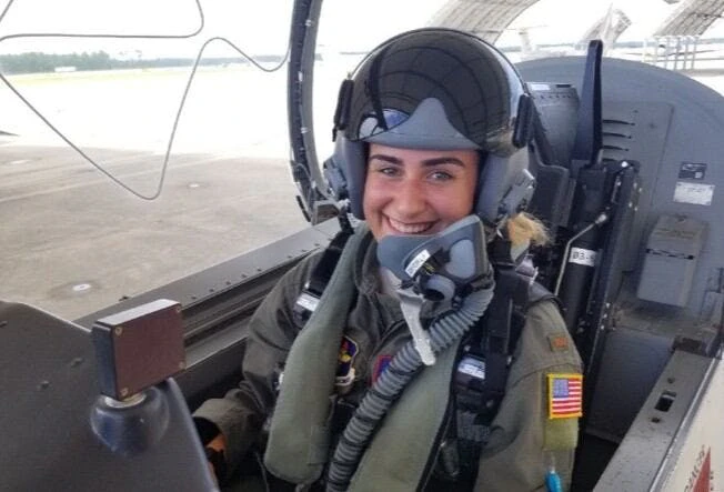 A woman wearing air force gear and a helmet sitting in the cockpit of an aircraft