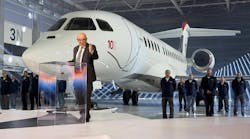 A man wearing a suit standing at a podium and speaking in front of a large white airplane with '10X' printed on the side A man wearing a suit standing at a podium and speaking in front of a large white airplane with '10X' printed on the side