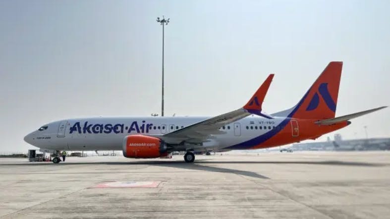 A white airplane with red accents on the tail and wings and text printed on the side that reads: Akasa Air