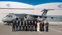 A group of professionals wearing business attire standing in front of a gray aircraft with 'Embraer KC-390 Millennium' printed on the side, with a building in the background labeled 'WZL-2' A group of professionals wearing business attire standing in front of a gray aircraft with 'Embraer KC-390 Millennium' printed on the side, with a building in the background labeled 'WZL-2'