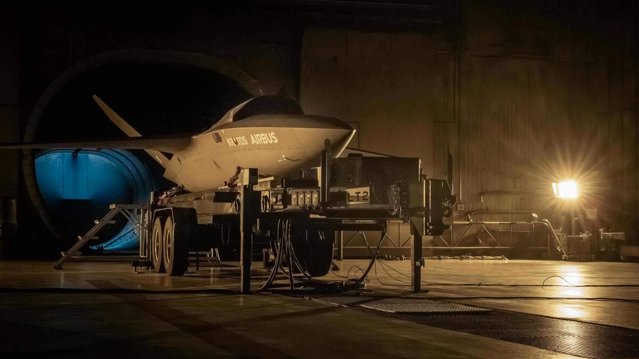 A dark scene of an aircraft with the word 'AIRBUS' printed on the side parked inside a hangar in dim lighting