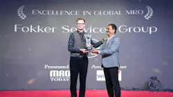 A man accepting an award from another man while on stage, standing in front of a backdrop that reads: Excellence in Global MRO Fokker Services Group A man accepting an award from another man while on stage, standing in front of a backdrop that reads: Excellence in Global MRO Fokker Services Group