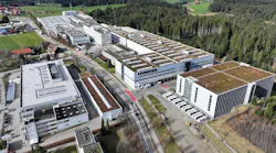 An aerial view of a facility campus with several large industrial buildings, roads and parking lots