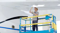 A technician standing on a blue lifted platform working on the wing of a white aircraft from underneath A technician standing on a blue lifted platform working on the wing of a white aircraft from underneath