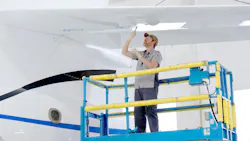 A technician standing on a blue lifted platform working on the wing of a white aircraft from underneath A technician standing on a blue lifted platform working on the wing of a white aircraft from underneath