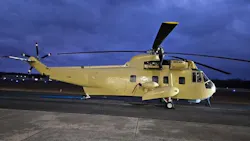 A beige helicopter parked on a tarmac in dim evening lighting