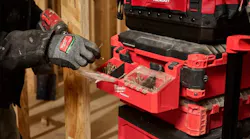 A gloved hand holding a nail next to a toolbox with a compartment on the side filled with nails and screws