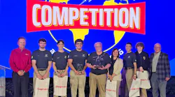 A group of young adults holding gift bags with one holding a trophy, standing in a line between older professionals, under a banner that reads: COMPETITION