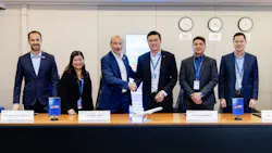 A group of professionals wearing suits and sitting at a table, with two men shaking hands while everyone smiles at the camera
