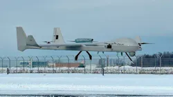 A large aircraft hovering above a tarmac, with a snow-covered ground and fence in the background A large aircraft hovering above a tarmac, with a snow-covered ground and fence in the background