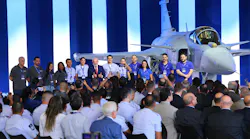 A line of people wearing blue polo shirts standing on stage in front of an airplane in front of a large crowd