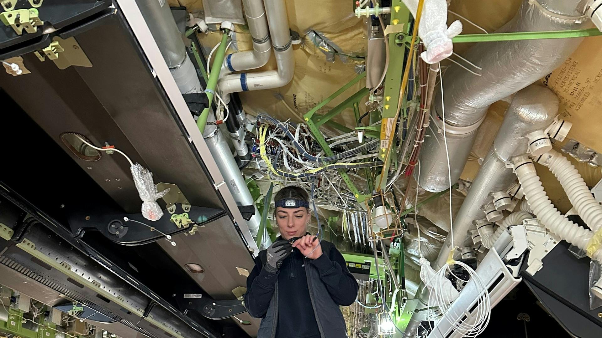 A technician working on electrical wires underneath an open ceiling with wires and ducts showing