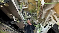 A technician working on electrical wires underneath an open ceiling with wires and ducts showing